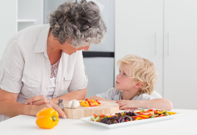 Little boy looking at his grandmother cooking at home